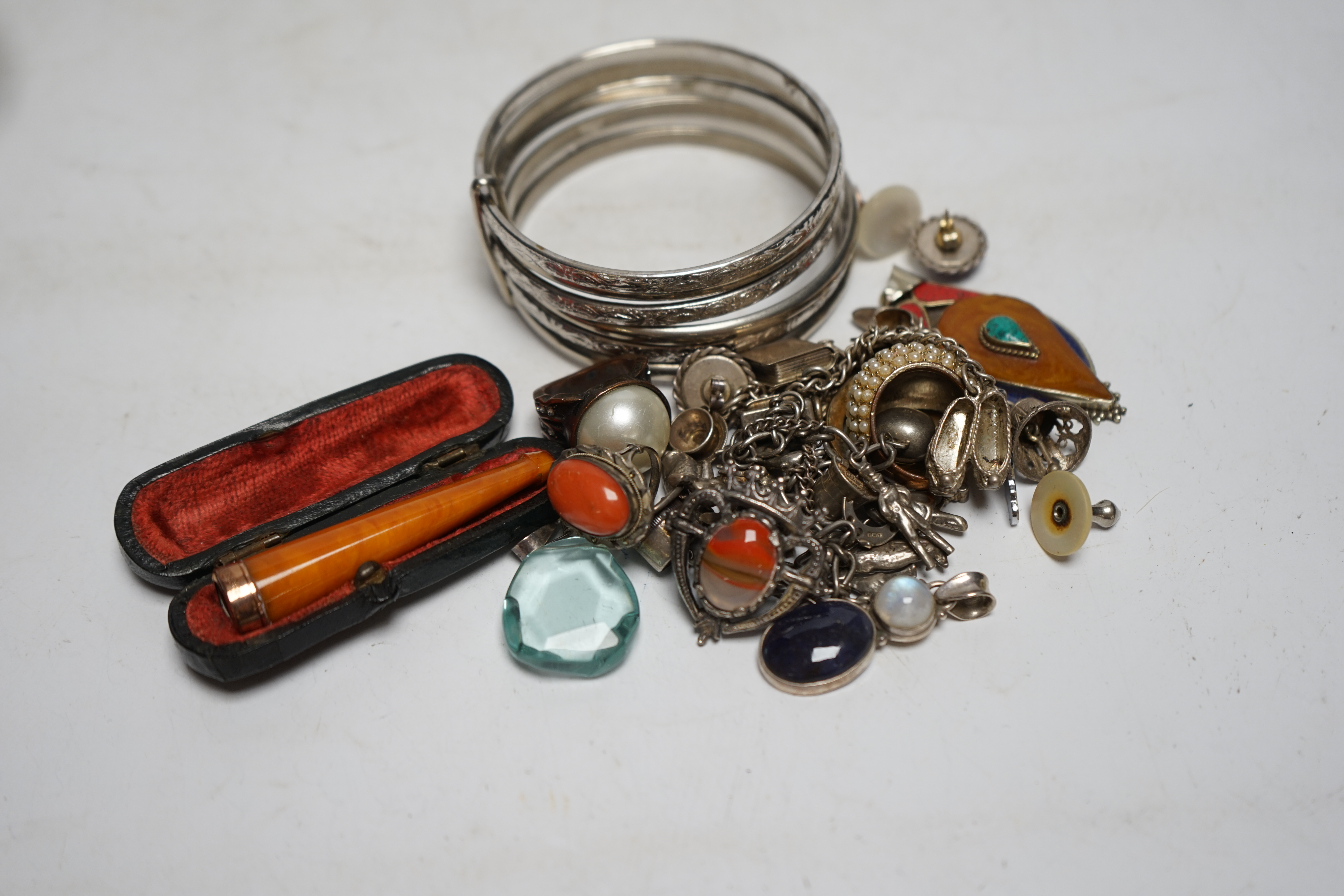 A small group of assorted white metal and costume jewellery including two charm bracelets and a cased 9ct gold mounted amber cigarette holder. Condition - poor to fair